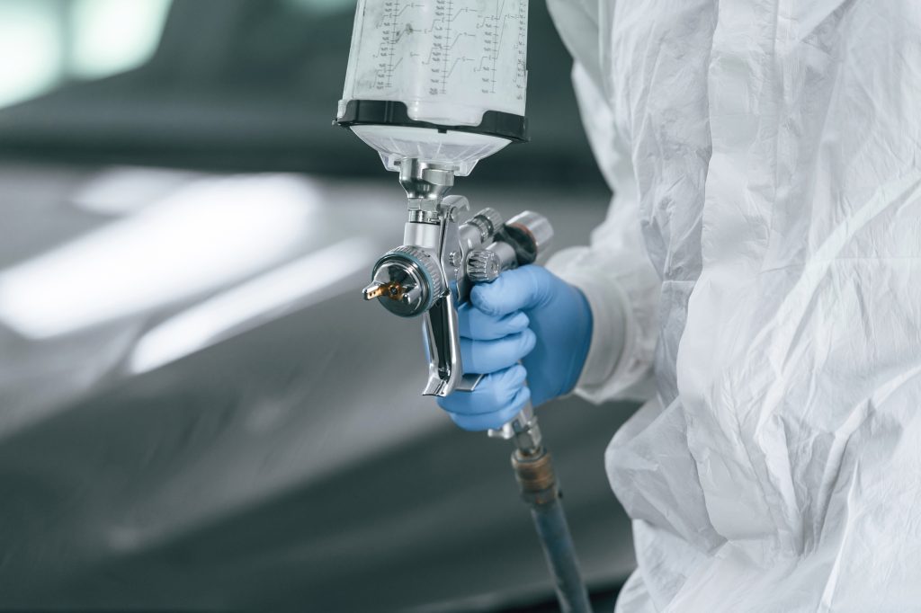 Focused close up view. Man is holding spray gun for painting a car